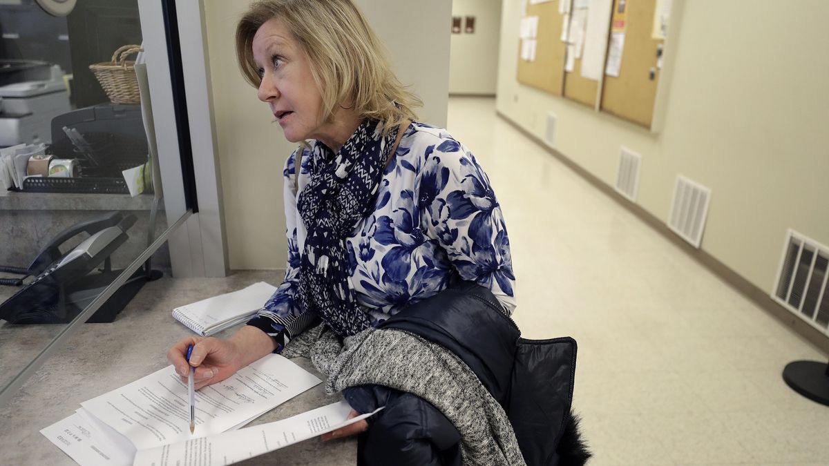 In this Thursday, Jan. 16, 2020 photo Jo Goode, city hall reporter for The Herald News of Fall River, Mass., picks up documents, at Fall River City Hall. Goode, who had reported extensively on the Fall River mayor's indictment on federal extortion charges, didn't expect that in 2018 the mayor would create an anonymous website, with her name as the address, featuring an endless loop of a video clip of President Donald Trump saying "You are fake news!" (AP Photo/Steven Senne)