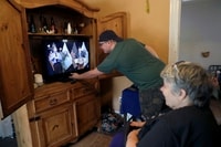 Image: Zach Stafford adjusts the TV volume at home in Belleville, Ill., on April 28 as he and his mother, Debra Mize, watch the daily coronavirus briefing by Illinois Gov. J.B. Pritzker (D).