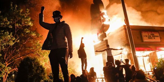 Protestors demonstrate outside of a burning fast food restaurant, Friday, May 29, 2020, in Minneapolis. Protests over the death of George Floyd, a black man who died in police custody Monday, broke out in Minneapolis for a third straight night. (AP Photo/John Minchillo)