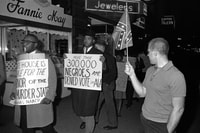 Image: A man holds a Confederate flag as others demonstrate in front of an Indianapolis hotel where Alabama Gov. George Wallace (D) was staying on April 14, 1964. The governor arrived in Indiana to campaign in the Democratic presidential primary.