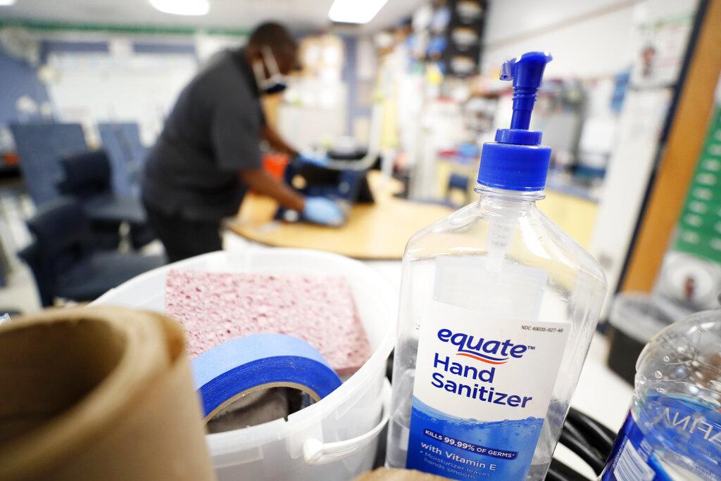 A bottle of hand sanitizer sits on a cart as Des Moines Public Schools custodian Tracy Harris cleans a chair in a classroom at Brubaker Elementary School, Wednesday, July 8, 2020, in Des Moines, Iowa.(AP Photo / Charlie Neibergall)